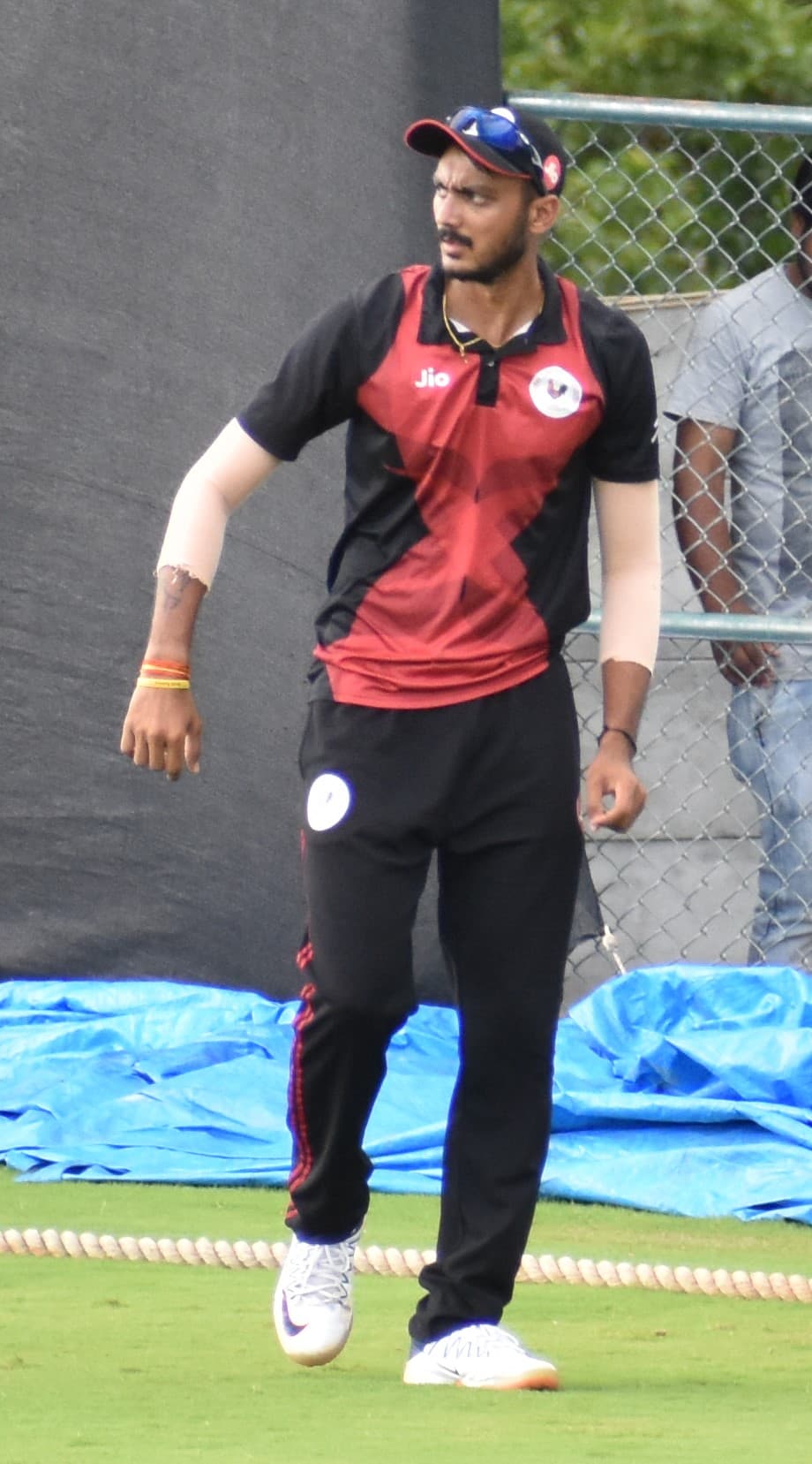 Axar Patel in Gujarat's red and black kit, walking in from the boundary rope.